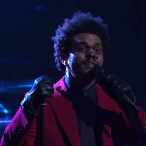 a man in a red jacket and black gloves is singing into a microphone on stage