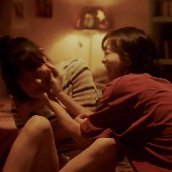 two women sitting on a bed laughing and looking into each other's eyes in a dimly lit room