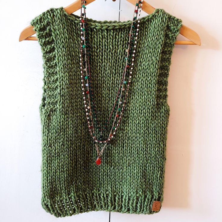 a green sweater with beads hanging from it's back on a wooden hanger