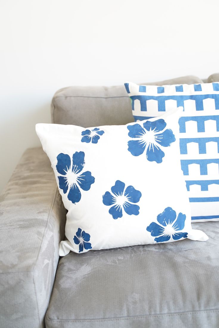 two blue and white pillows sitting on top of a gray couch next to a wall