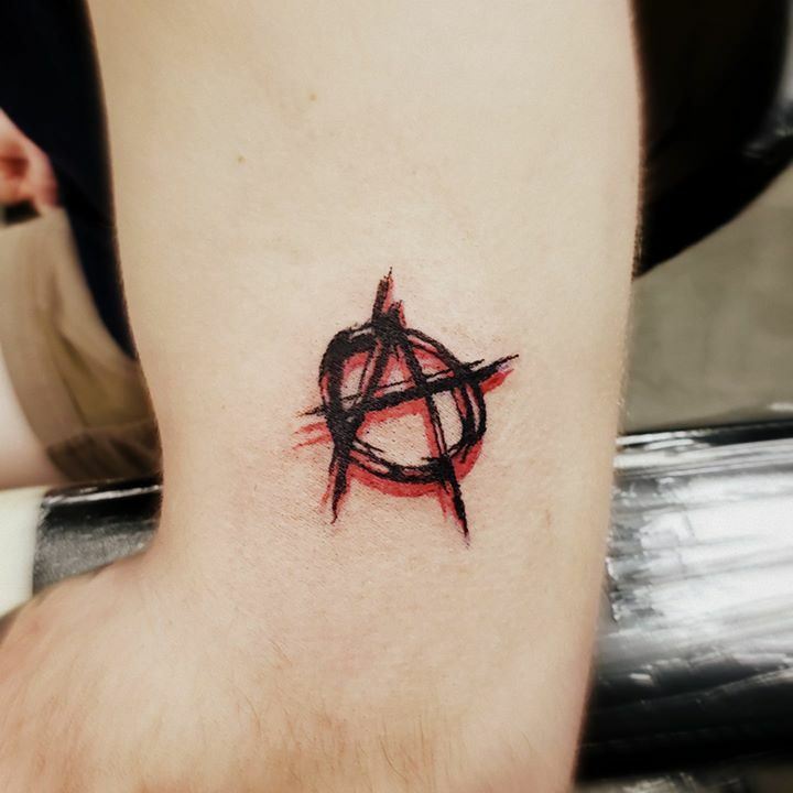 a small tattoo on the ankle of a man's foot, depicting an anarchy symbol