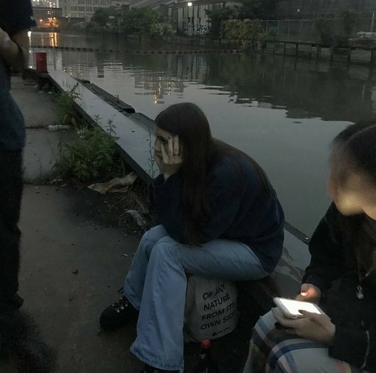 two people sitting next to each other on the side of a body of water with buildings in the background