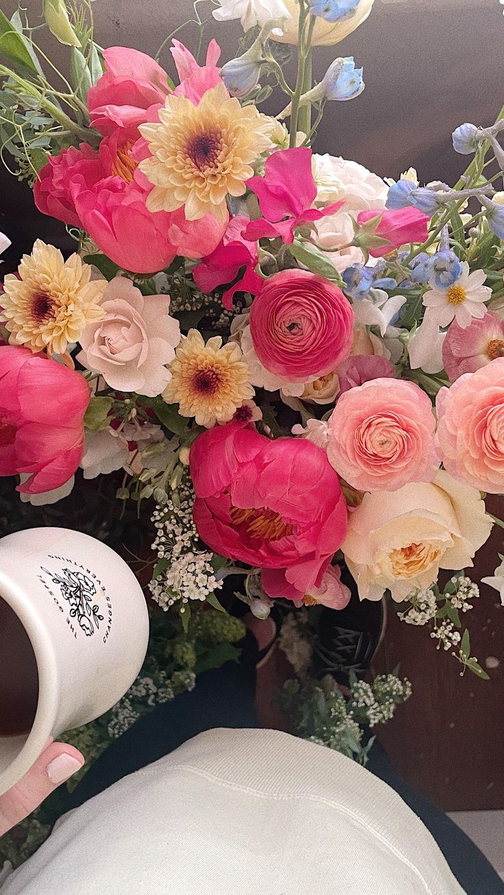 a person holding a coffee cup next to a bouquet of flowers