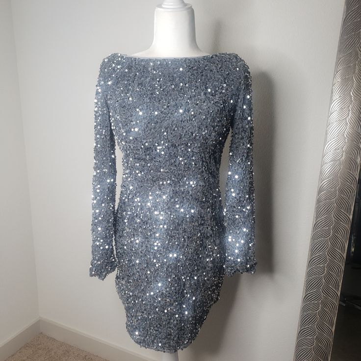 Grey/Silver Sequin Dress Lined Long Sleeves Mini Split In Front Open Back With Tie Invisible Zipper In Back You Will Steal The Show In Our Gorgeous Demure Dress. We Are Obsessed With That Sparkly Sequin Fabric And Open Back Feature. Perfect For A Special Birthday Occasion Or A Night Out With Your Bff's. Team It With Clear Heels For A Super Hot Look. Silver Embellished Sequin Dress For Holiday, Holiday Silver Embellished Sequin Dress, Silver Fitted Long Sleeve Mini Dress, Silver Sequin Glitter Dress For Evening, Silver Long Sleeve Embellished Mini Dress, Silver Long Sleeve Sequined Dress, Long Sleeve Silver Sequined Mini Dress, Silver Embellished Long Sleeve Mini Dress, Silver Long Sleeve Winter Dress