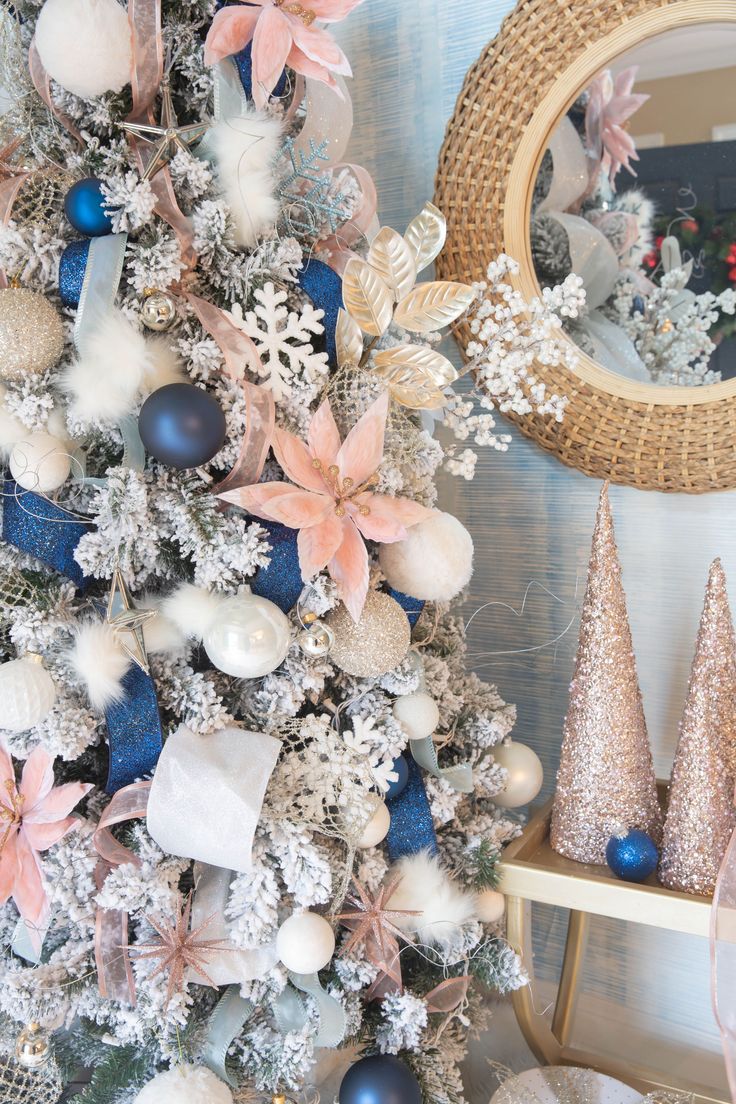 a christmas tree decorated with blue, white and pink ornaments in front of a mirror