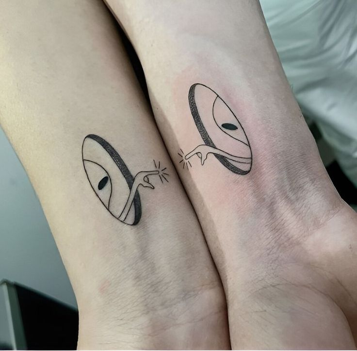 two people with matching tattoos on their arms, one has an alien face and the other has a cat