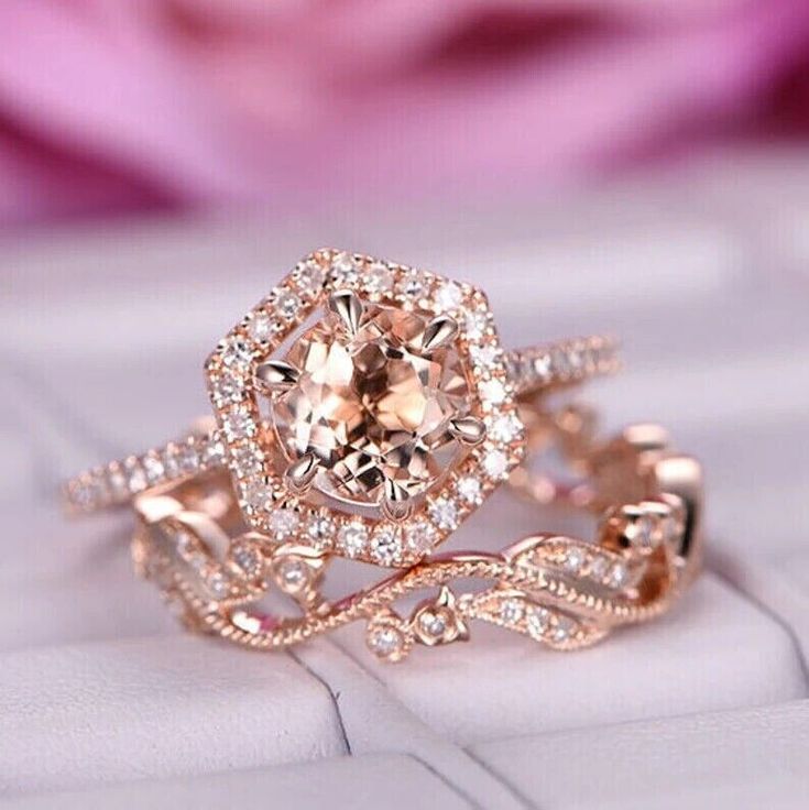 a close up of a diamond ring on top of a white surface with pink flowers in the background