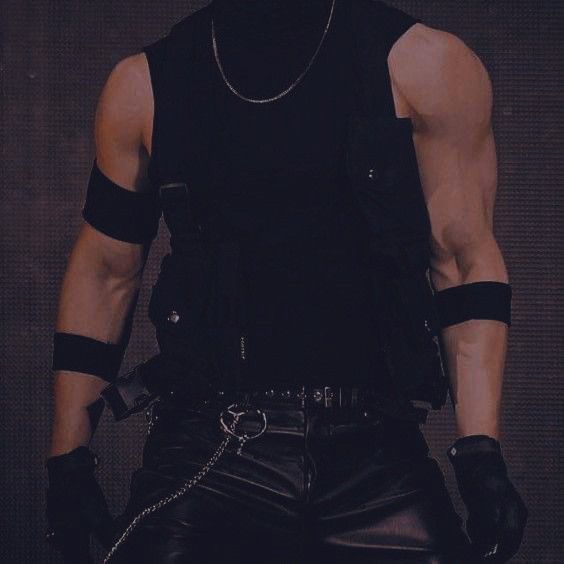 a man in leather pants and a black shirt with chains on his chest, wearing a chain around his neck