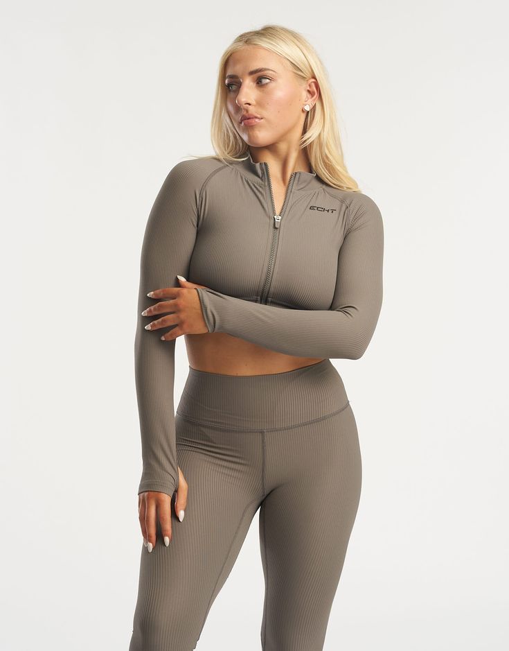 The Rise series awakes - taking ECHT's seamless fabric to a new level. This cropped long sleeve is made of a soft and flexible ribbed fabric and sits comfortably across the waist to accentuate your silhouette. Featuring full zip from collar to waist to keep you warm or cool, thumb holes and advanced heat pressed silicone ECHT logo. The Rise Zip up long sleeve paired with marching Rise Leggings is suitable for all day wear and low intensity workouts. - Seamless fabric with a ribbed structure - Sweat-wicking and breathable - Super soft peach-like sensation feel - Thumb holes to keep fingers warm - Cropped waist length - Zip from collar to waist 76% Nylon, 24% Spandex Phoebe is wearing a Small, and is 5'4" Seamless Fitted Long Sleeve Activewear, Stretch Long Sleeve Crop Top With Thumbholes, Long Sleeve Stretch Crop Top With Thumbholes, Long Sleeve Stretch Crop Top, Ribbed Long Sleeve Stretch Crop Top, Ribbed Long Sleeve Sports Activewear, Ribbed Long Sleeve Activewear For Workout, Fall Workout Long Sleeve Crop Top, Ribbed Long Sleeve Crop Top With High Stretch