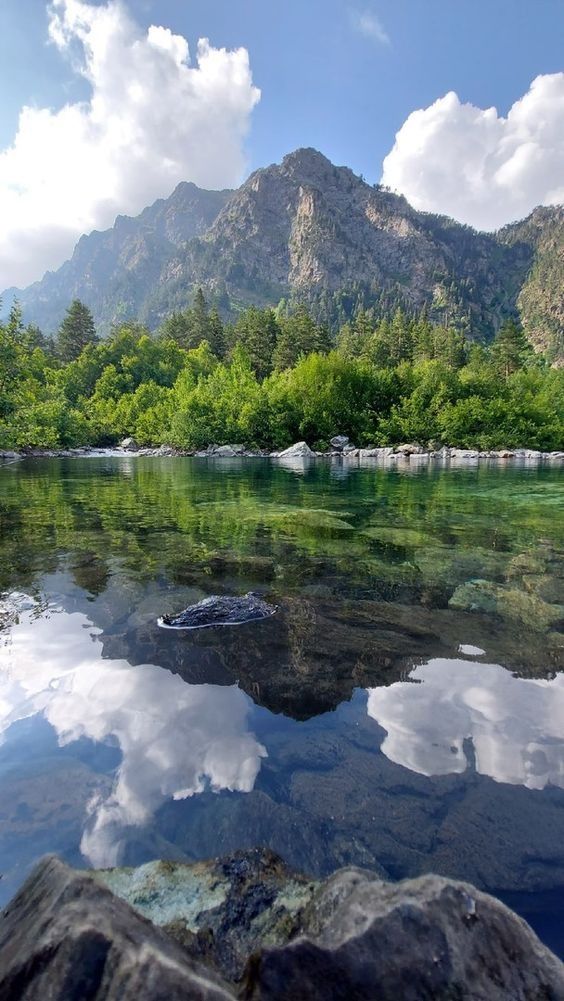 the water is very clear and blue with clouds in the sky above it, as well as mountains