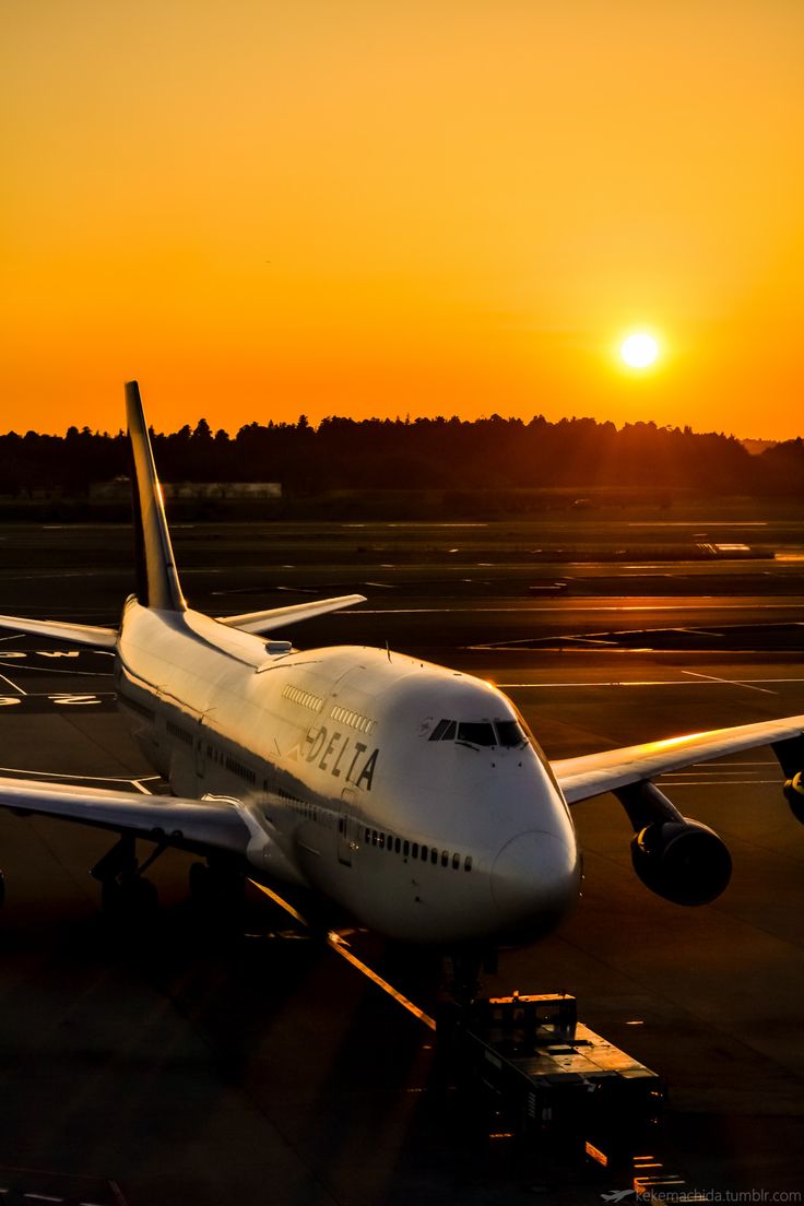 an airplane is sitting on the runway as the sun goes down in the distance behind it