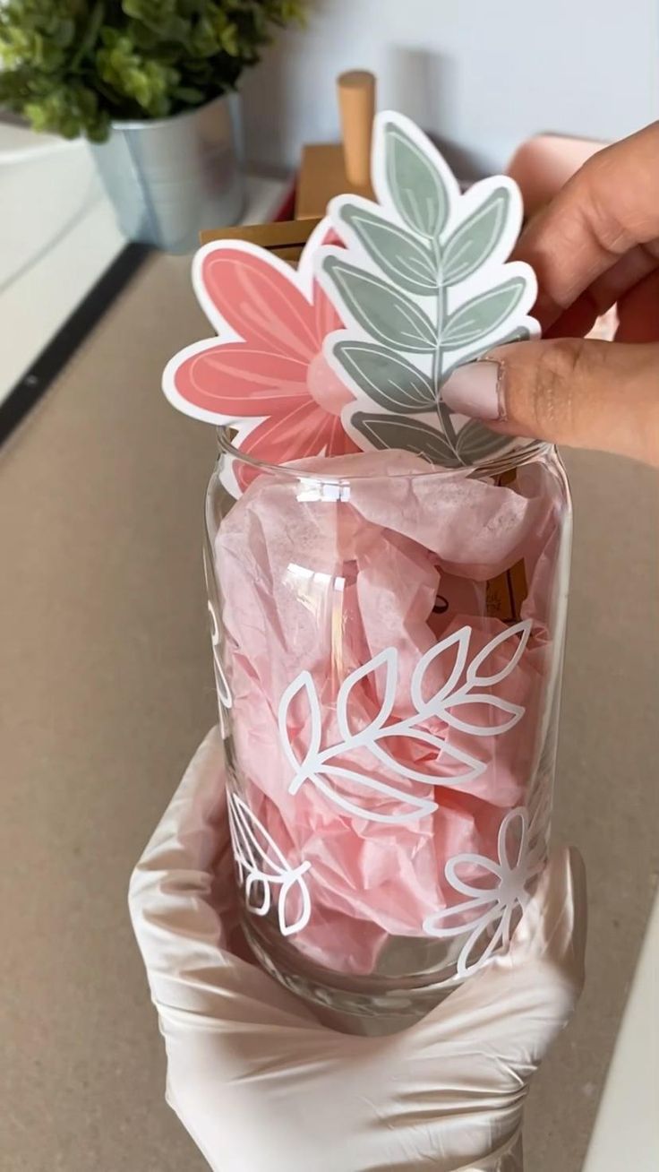 a person is holding a glass with some pink tissue paper in it and there are leaves on top