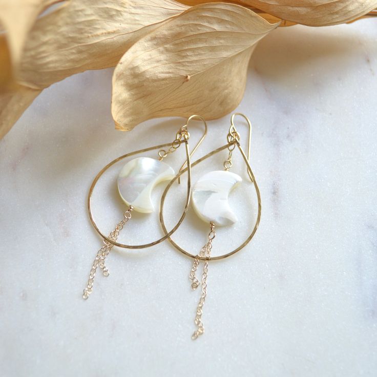 Mother of pearl crescent moon dangle within 19g hammered teardrops in either gold filled or sterling silver. Crescents are 15x12mm Teardrops are approximately 40mm long. Elegant Hammered Crescent Earrings, Teardrop 14k Gold-filled Pearl Earrings For Anniversary, Teardrop 14k Gold Filled Pearl Earrings For Anniversary, 14k Gold Filled Teardrop Pearl Earrings For Anniversary, Delicate Nickel-free Teardrop Pearl Earrings, Delicate Teardrop Pearl Earrings Nickel-free, Teardrop Mother Of Pearl Ear Wire Jewelry, Teardrop Pearl Charm Earrings In 14k Gold, Delicate Teardrop Pearl Earrings Nickel Free