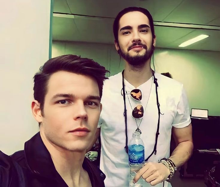 two men standing next to each other in an office building, one holding a water bottle and the other looking at the camera