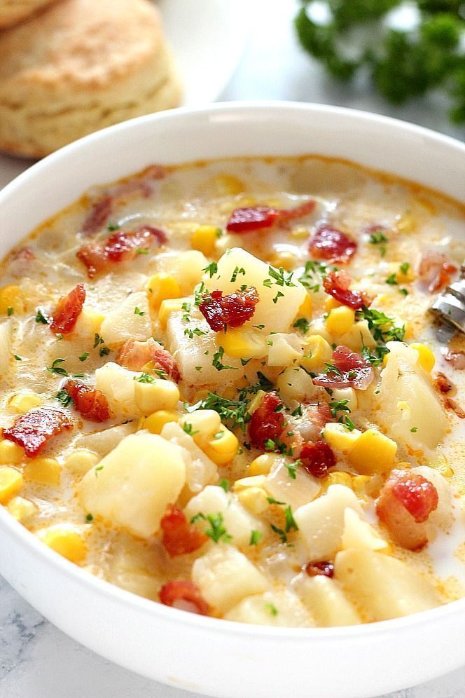 a white bowl filled with corn and potato chowder next to crackers on the side