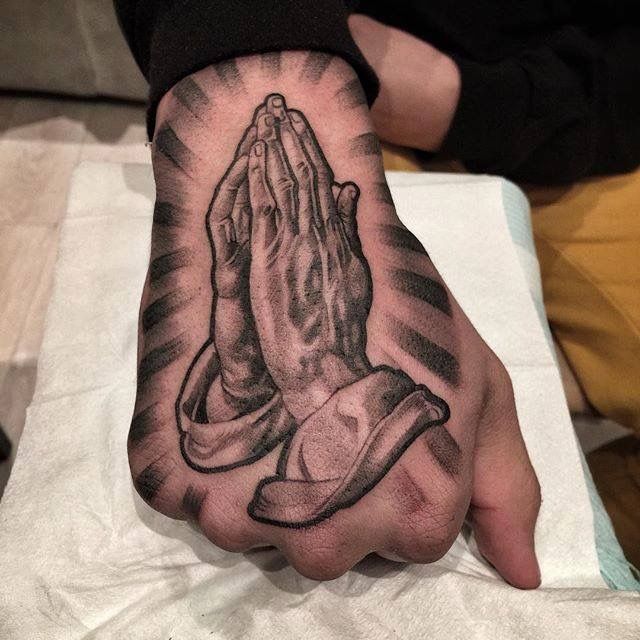 a person's hand with a tattoo on it and praying hands in the middle