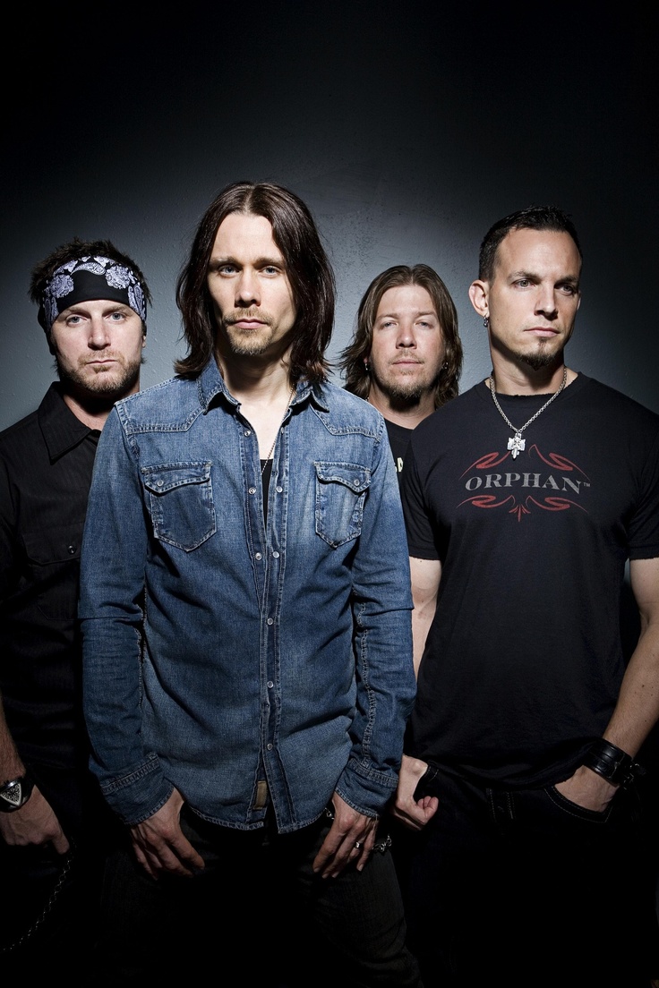 five men standing in front of a black background with one man wearing a bandana