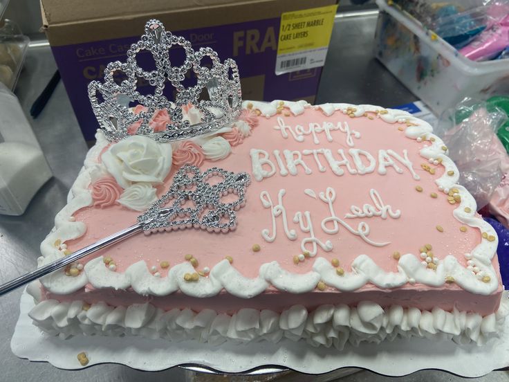 a birthday cake decorated with pink frosting and a tiara on top, sitting on a table