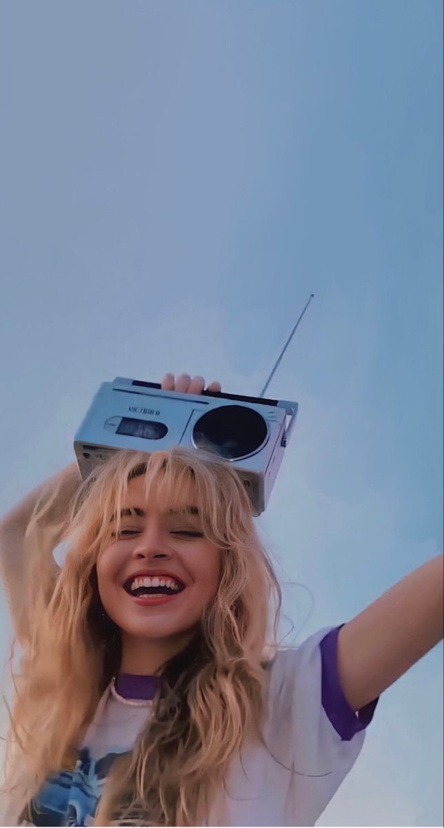 a woman with long blonde hair is holding a radio on her head and smiling at the camera