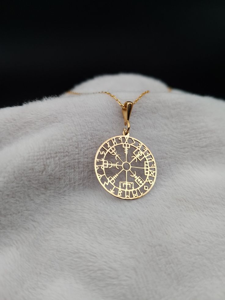 a gold plated necklace with a compass on it's back end, sitting on top of a white blanket