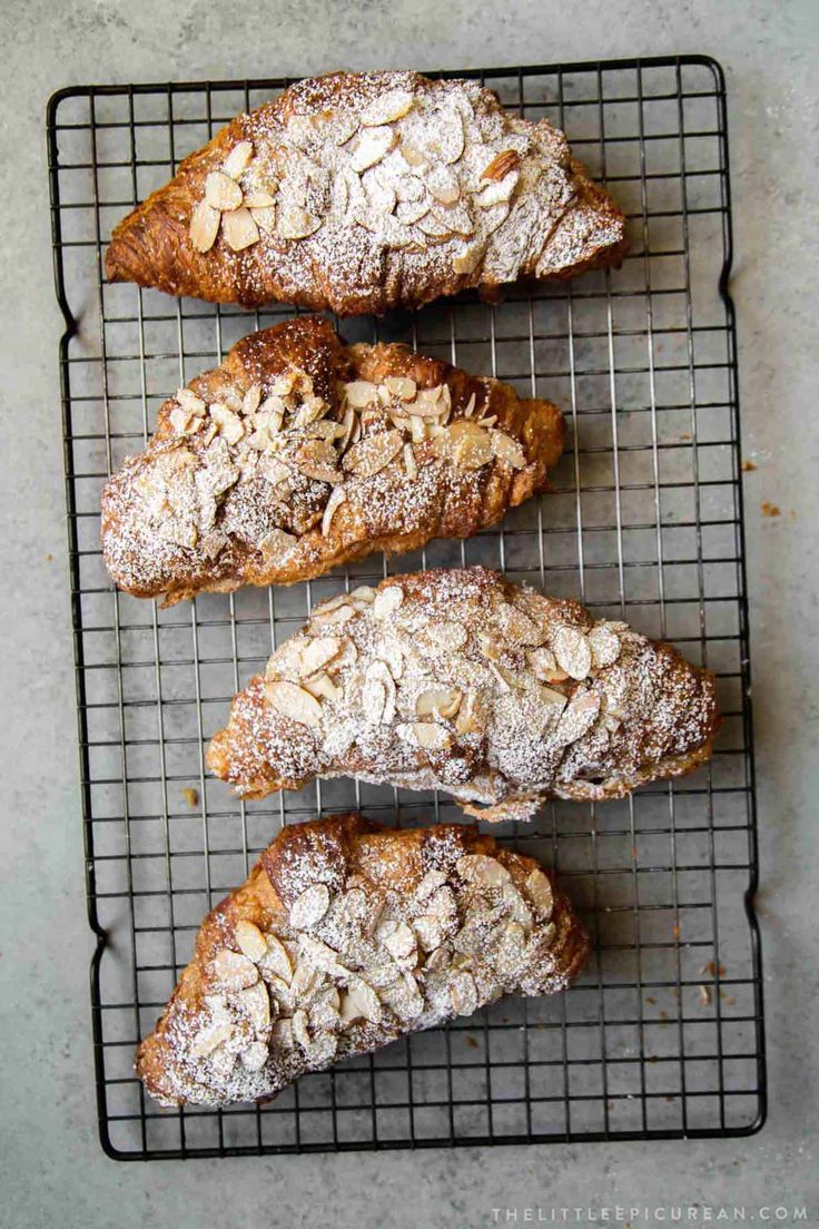 four pastries cooling on a wire rack with powdered sugar and almond toppings