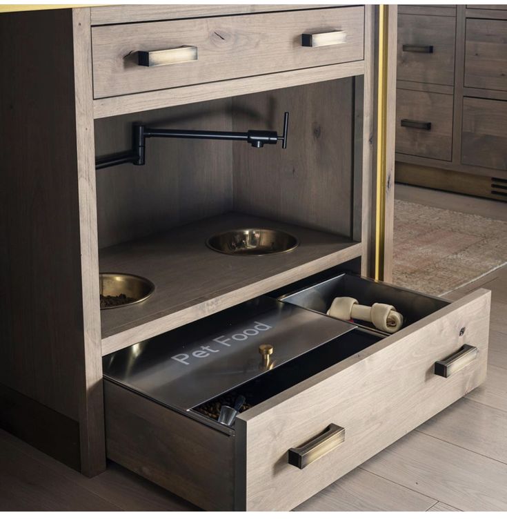 an open cabinet with two bowls and one dog bowl on the bottom, in a kitchen