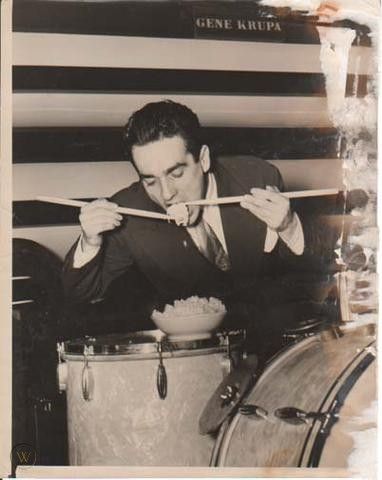 a man in a suit and tie is playing the drums while another man looks on