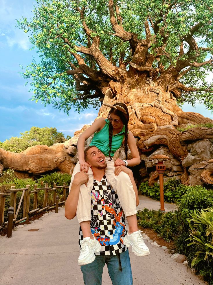 a man carrying a woman on his shoulders in front of a tree at disney's animal kingdom