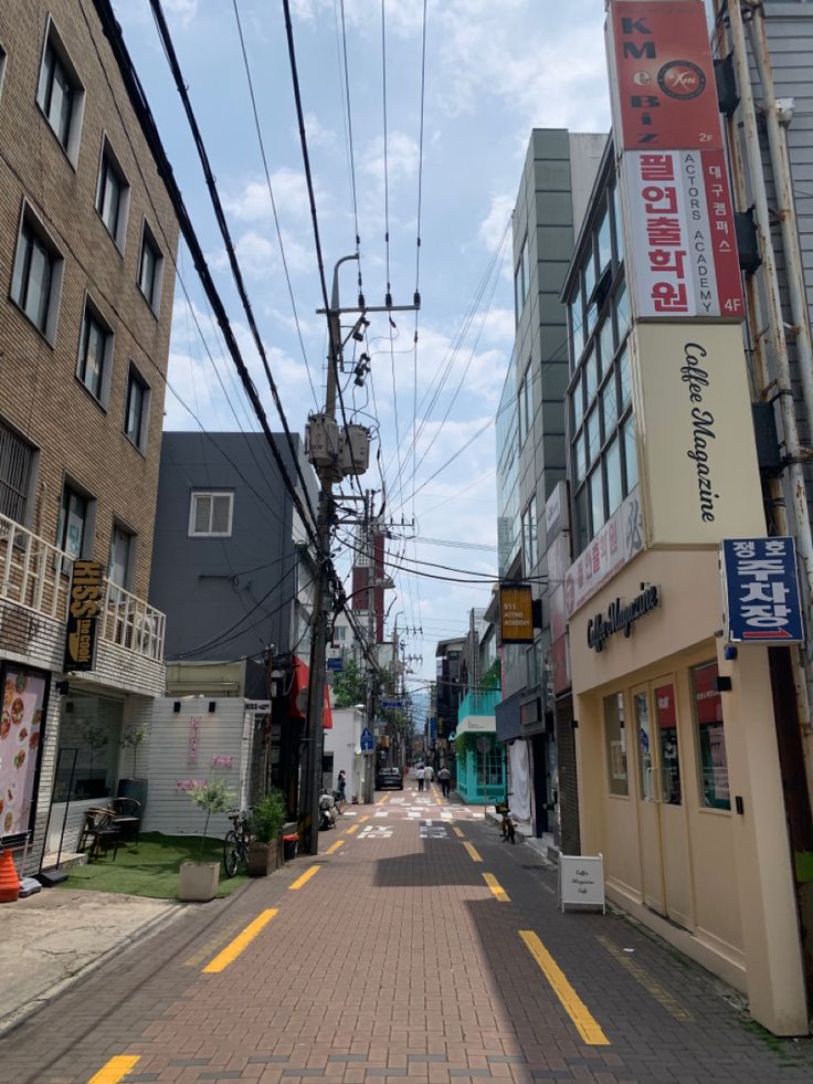 an empty city street lined with buildings and power lines above it is a yellow line painted on the sidewalk