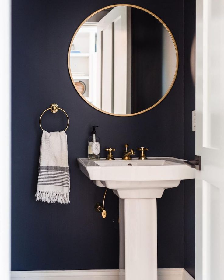 a white sink sitting under a round mirror in a bathroom next to a wall mounted faucet