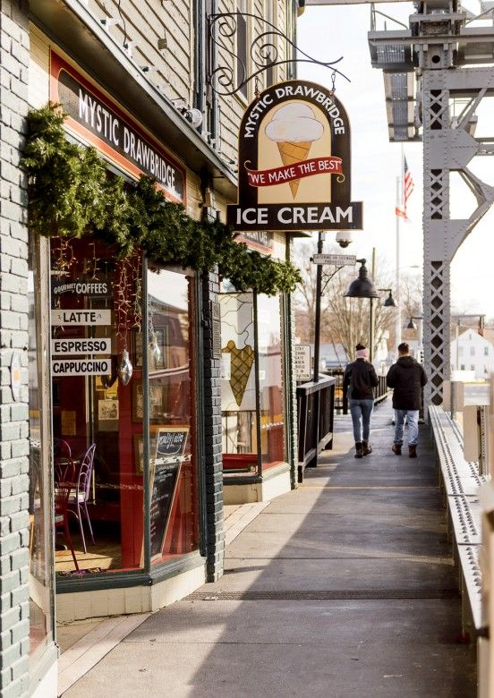 two people walking down the sidewalk in front of ice cream shops