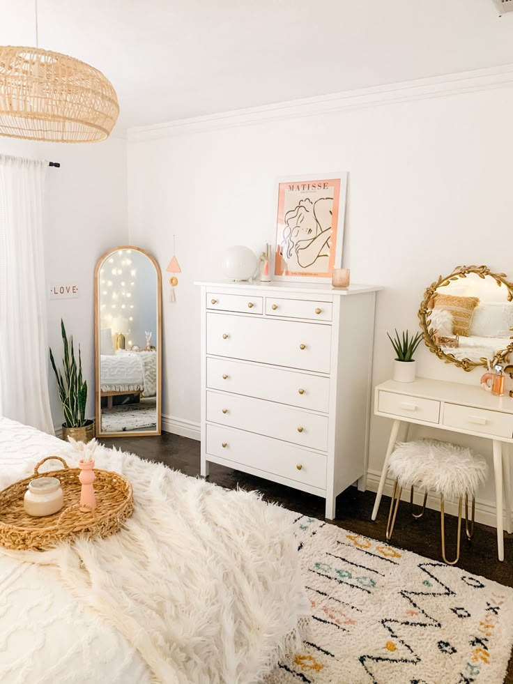 a bedroom with a white bed, dresser and mirror on the wall next to it