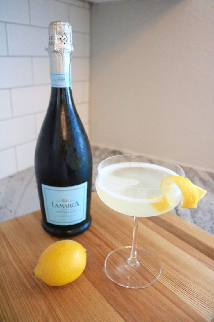 a bottle of champagne next to a glass filled with liquid and lemons on a wooden table