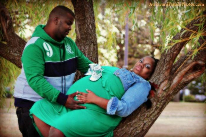 a pregnant woman laying on top of a tree next to a man in a green jacket