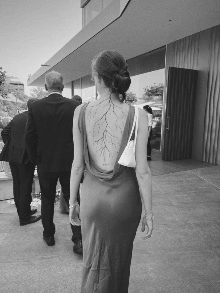 a woman in a dress walking down a sidewalk with her back to the camera and two men behind her