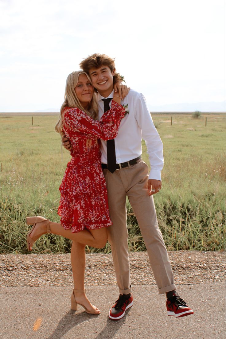 a man and woman posing for a photo in front of an open field with grass