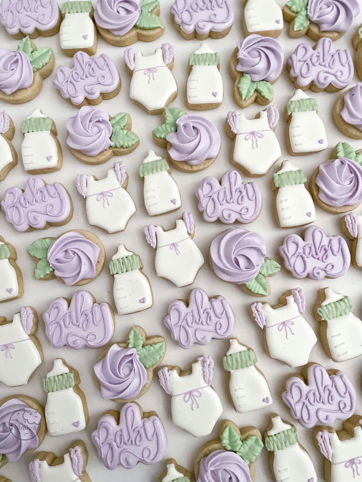 some cookies are decorated with purple and white icing for baby shower decorations on a table