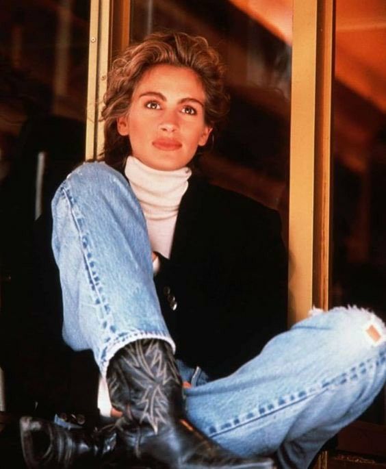 a woman sitting on the window sill with her legs crossed and wearing black boots