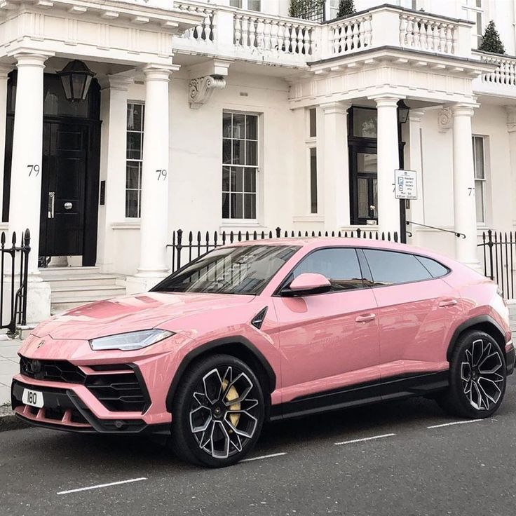 a pink lamb suv parked in front of a white building with black rims and gold accents