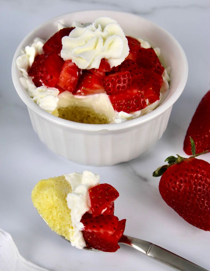 a bowl filled with cake and strawberries on top of a white counter next to a spoon