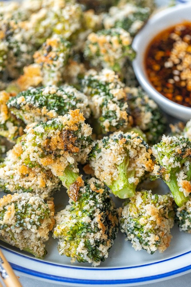 broccoli florets are on a plate with dipping sauce in the background