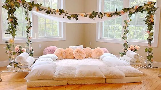 a bed with pillows and flowers on it in front of two large windows at the same time