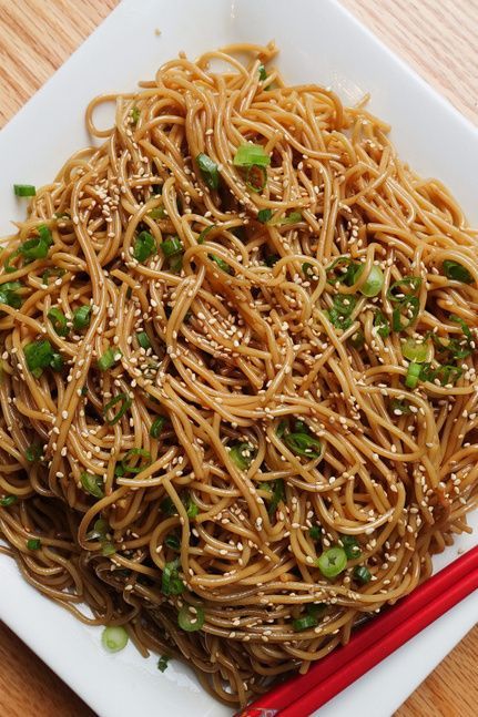 a white plate topped with noodles and chopsticks on top of a wooden table