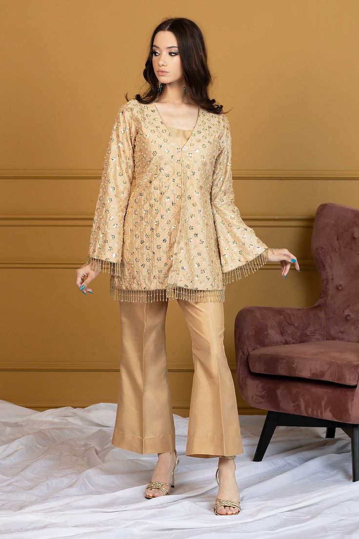 Model: 5'5 - 168 cm and 110 lbs - 50 kg size S Maria Nasir breathes life in this matte gold attire with her ingenious innovation. Rendered with crisp sequin details all over the raw silk gold ensemble with small sequin bunches symmetrically worked with threads. Siara is short gold jacket design with silk inner and bell-sleeves trimmed embellished tassel borders. The look completes with similar matte gold hued bell bottoms. This Pakistani fusion dress style is perfect to reveal your bold and desi expressions. Top: Color: Light Gold Fabric: Raw silk  Short jacket with sequins work all over  Silk lining inside  Bell shaped full sleeves  Dangling tassles  V-neck Bottom: Color: Light Gold   Fabric: Silk Bell bottom pants Half elasticated waist Bell Bottom Sleeves Pakistani, Bell Bottom Suits Pakistani, Bollywood Silk Palazzo Set With Sequins, Eid Silk Sequined Palazzo Set, Gold Palazzo Set In Raw Silk With Mirror Work, Gold Palazzo Set With Mirror Work In Raw Silk, Gold Silk Palazzo Set For Diwali, Gold Silk Palazzo Set With Zari Work, Festive Semi-stitched Sequined Palazzo Set