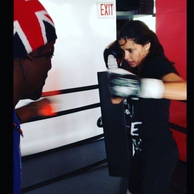 a woman in black shirt and boxing gloves standing next to a man wearing red hat