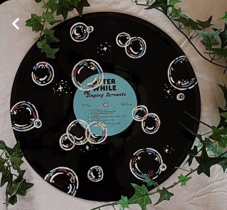 a black record with bubbles on it sitting next to some green leaves and ivys