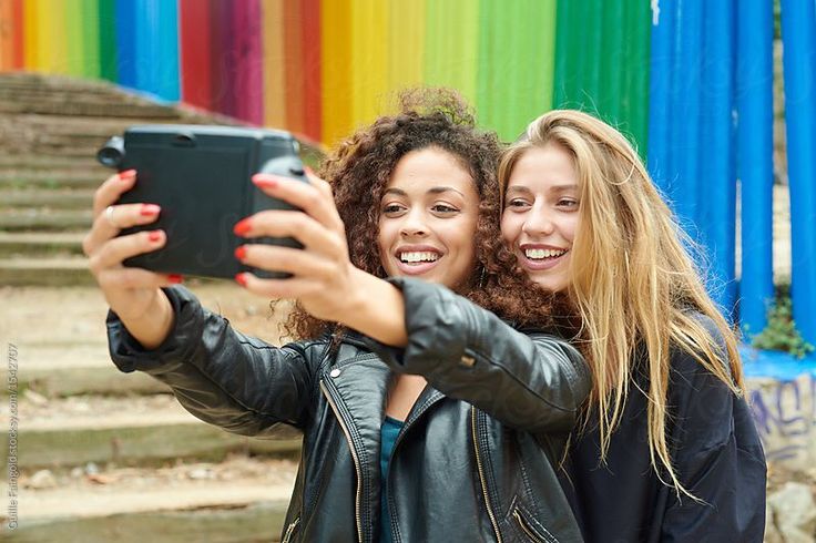 two young women taking a selfie in front of a rainbow - colored wall with their cell phone