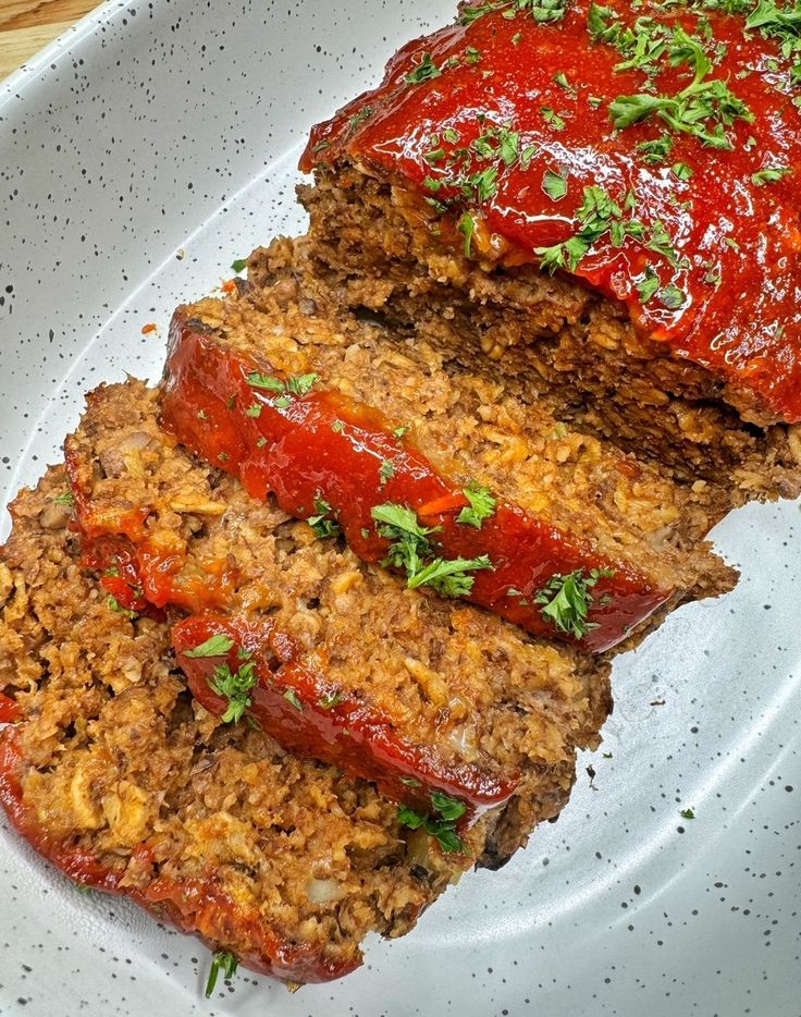 sliced meatloaf on a plate with sauce and parsley sprinkled on top