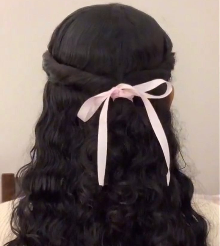 the back of a woman's head with long curly hair and a pink bow