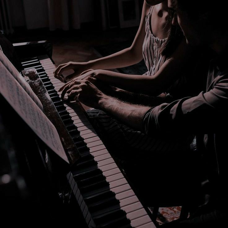 two people sitting at a piano in the dark with their hands resting on the keyboard